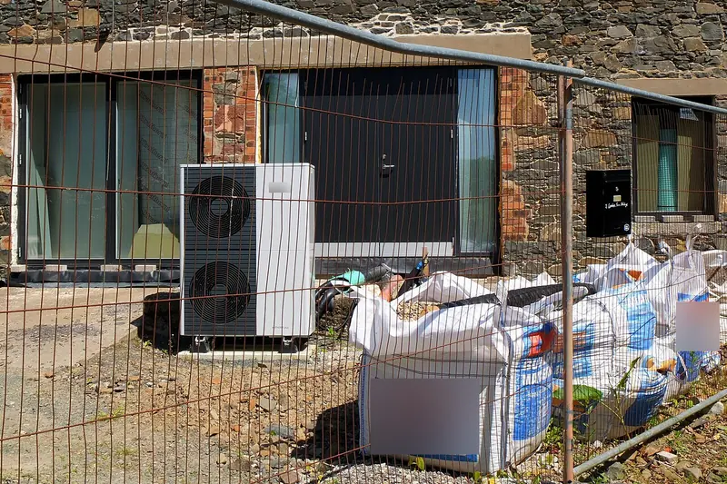 Twin-fan heat pump outdoor unit newly set in front of a stone building under renovation