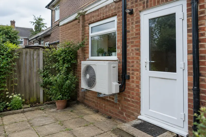 Outdoor heat pump unit on a wall bracket at the back of a brick semi-detached house