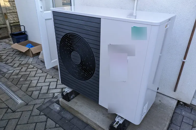 New white air source heat pump on a concrete plinth beside the back door of a terraced house