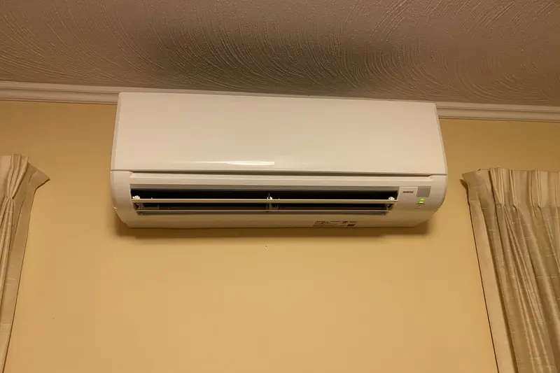 White wall-mounted split air-conditioning unit high on a cream wall between curtains