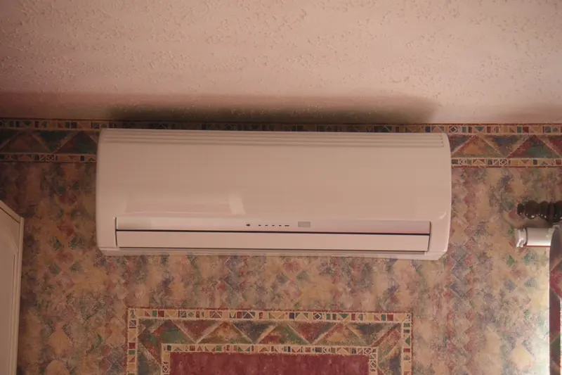 Older wall-mounted split air-conditioning unit in a room with patterned wallpaper